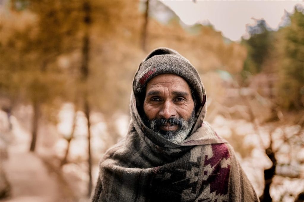 Un pastore avvolto in una coperta sorride in un bosco autunnale. La felicità secondo Epicuro è vivere con poco, senza paura.